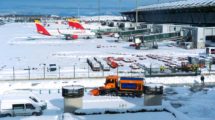 Barajas cubierto de nieve y una máquina quitanieves actuando en un parking de vehículos del aeropuerto.