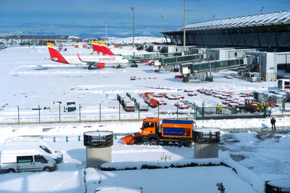Barajas cubierto de nieve y una máquina quitanieves actuando en un parking de vehículos del aeropuerto.